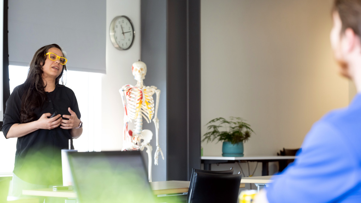 person standing and talking in a room with medical human skeleton in background