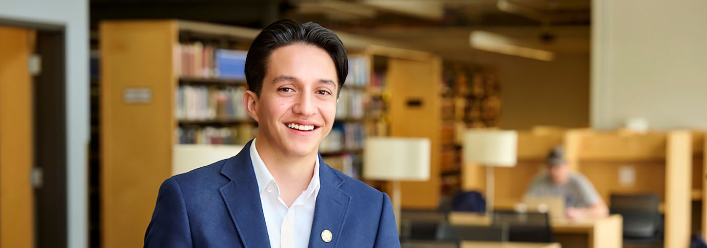 Student standing in a library looking at the camera smiling.